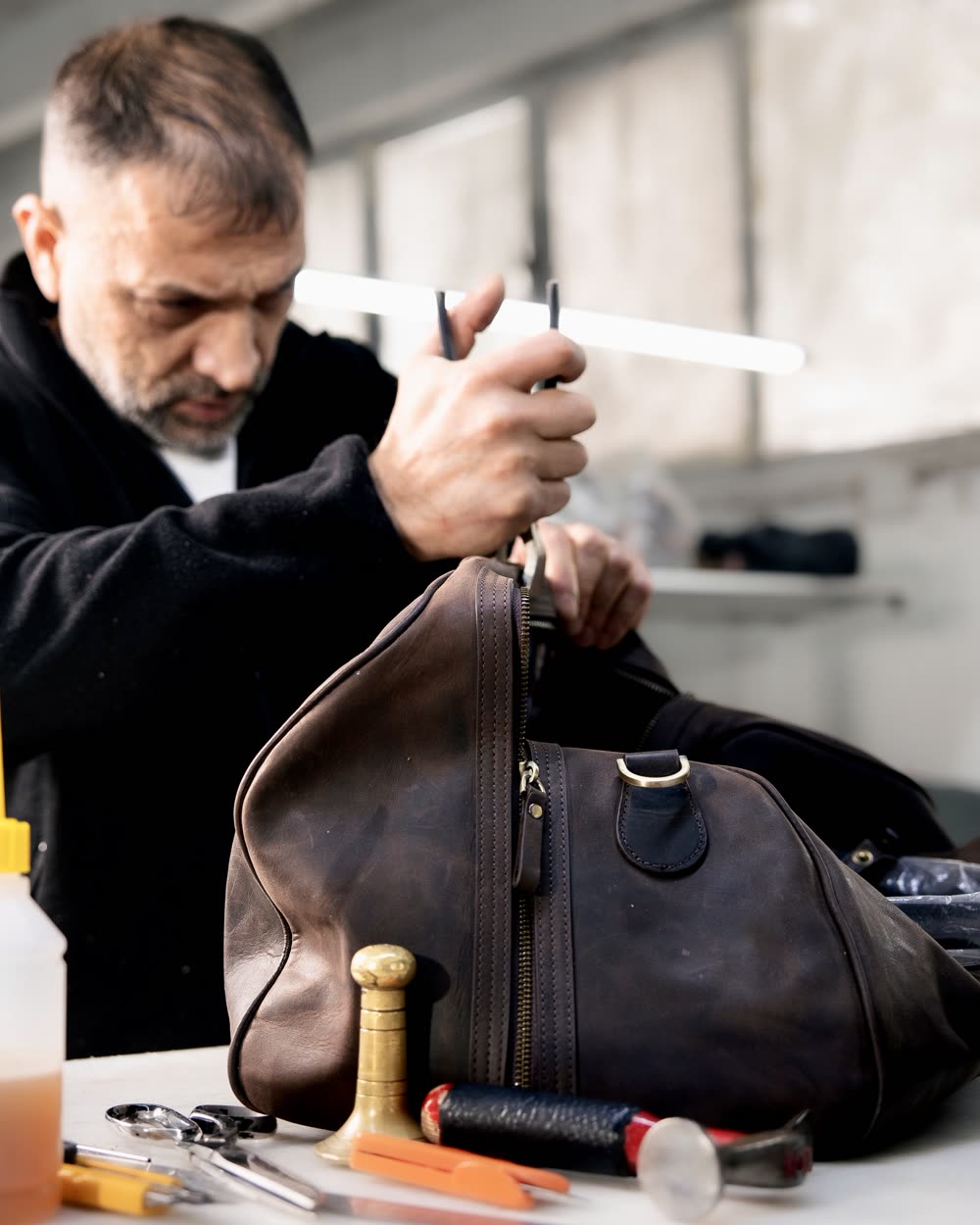 A craftsman finishing a leather bag in the workshop